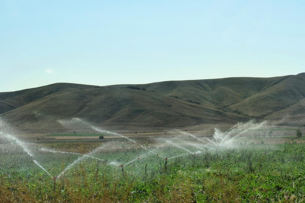 A vibrant sprinkler irrigation system in action across lush cropland and rolling hills.